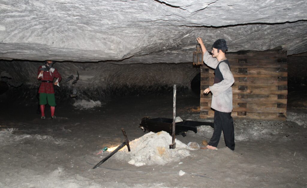 Element trasy turystycznej w Grotach Nagórzyckich – ekspozycja z figurą diabła, chłopa i kupką piasku, inspirowana lokalną legendą o diable nagórzańskim.